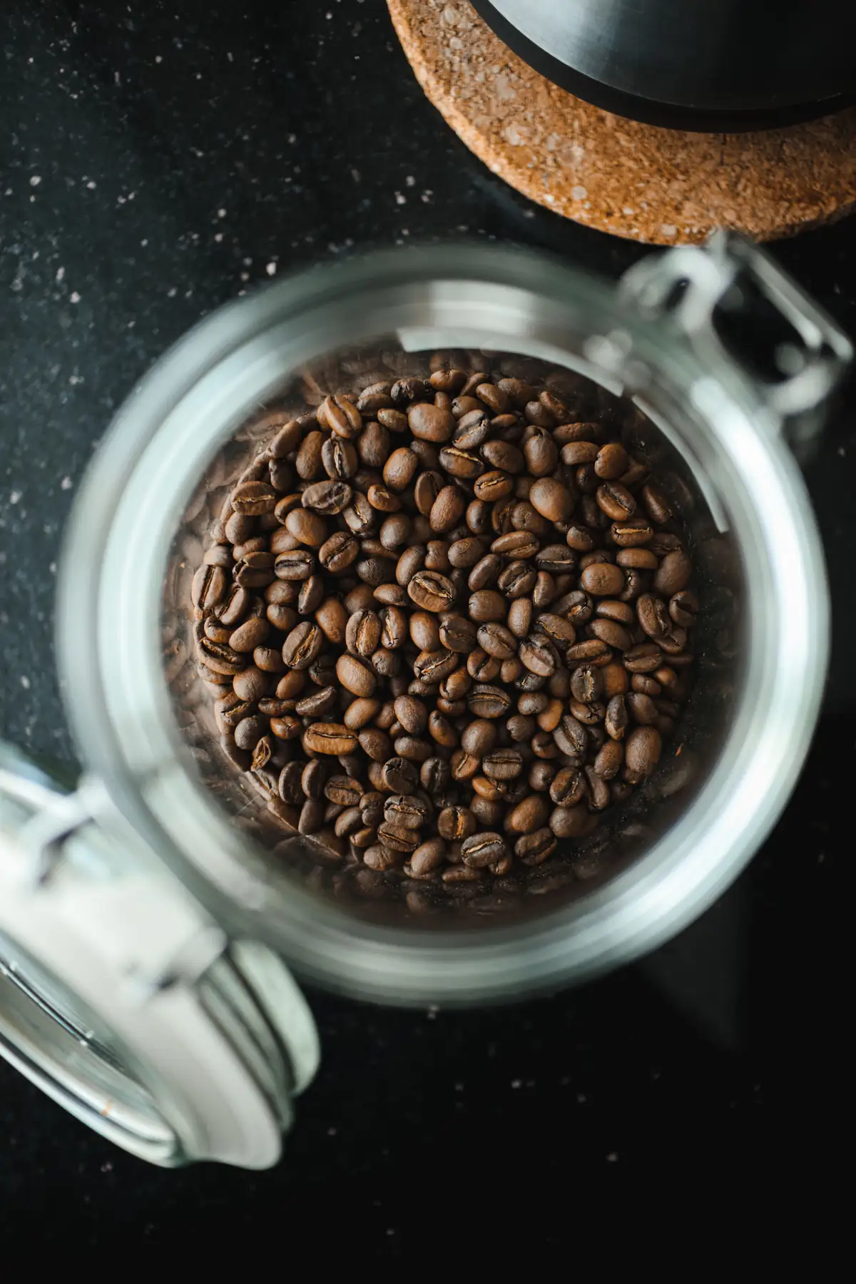 Roasted coffee beans stored in an open airtight glass jar, overhead view