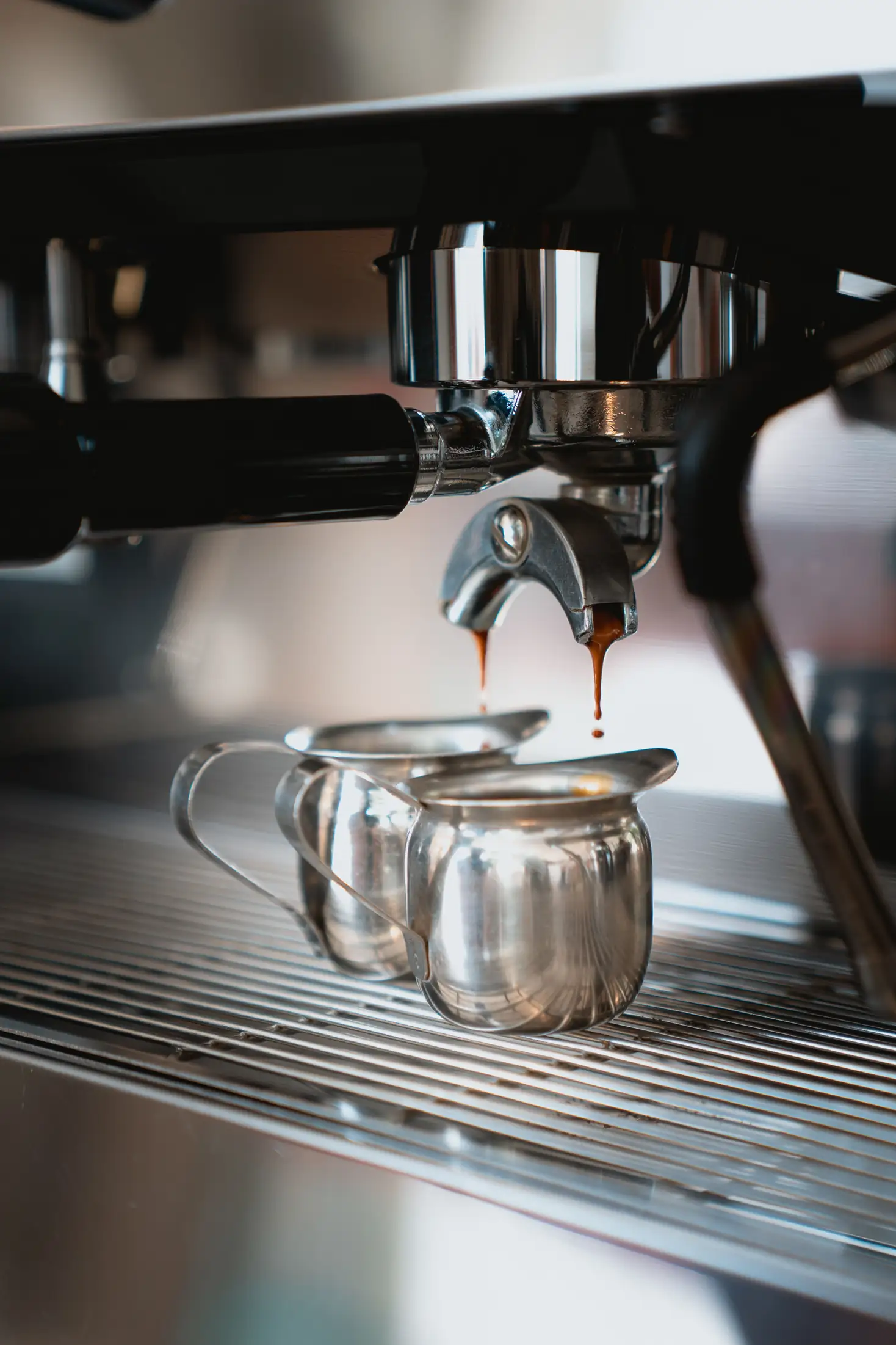 Close-up of an espresso machine's portafilter pouring two shots of espresso into small metal cups