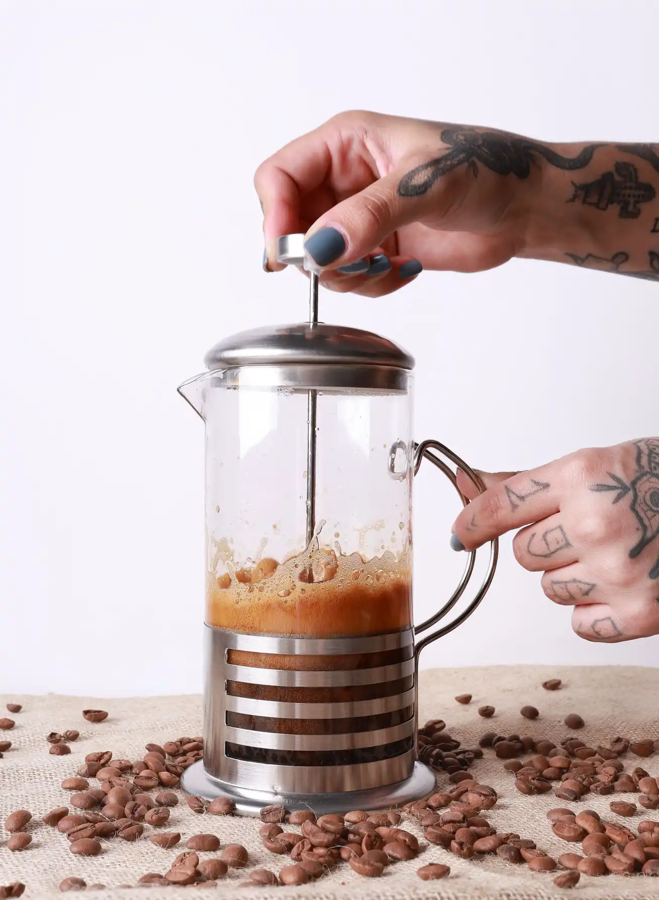 Hands operating a French press, coffee beans scattered around the base
