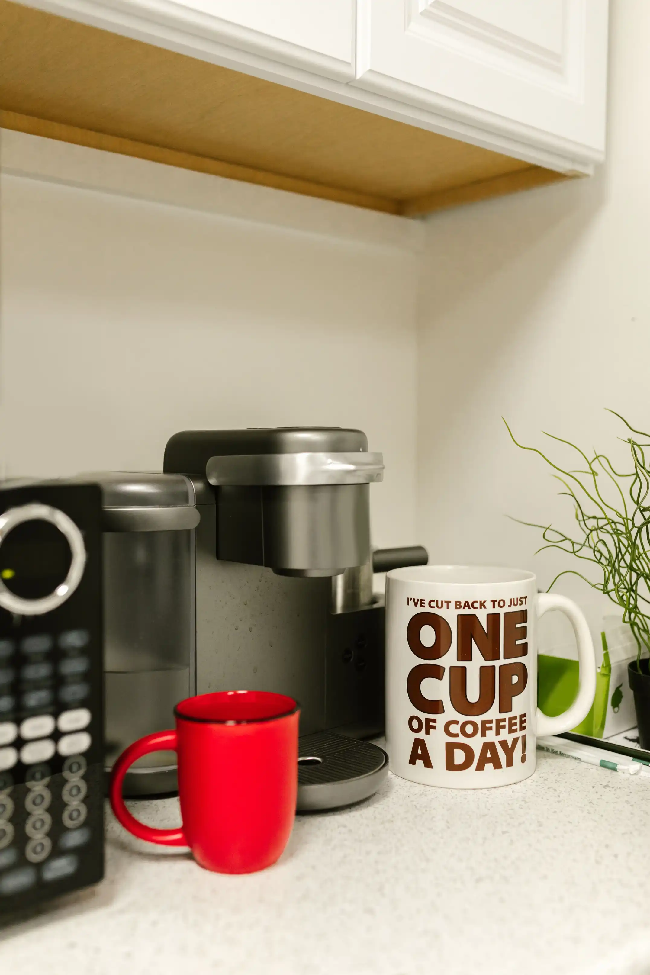 A black single-serve pod coffee machine on a kitchen counter next to two mugs